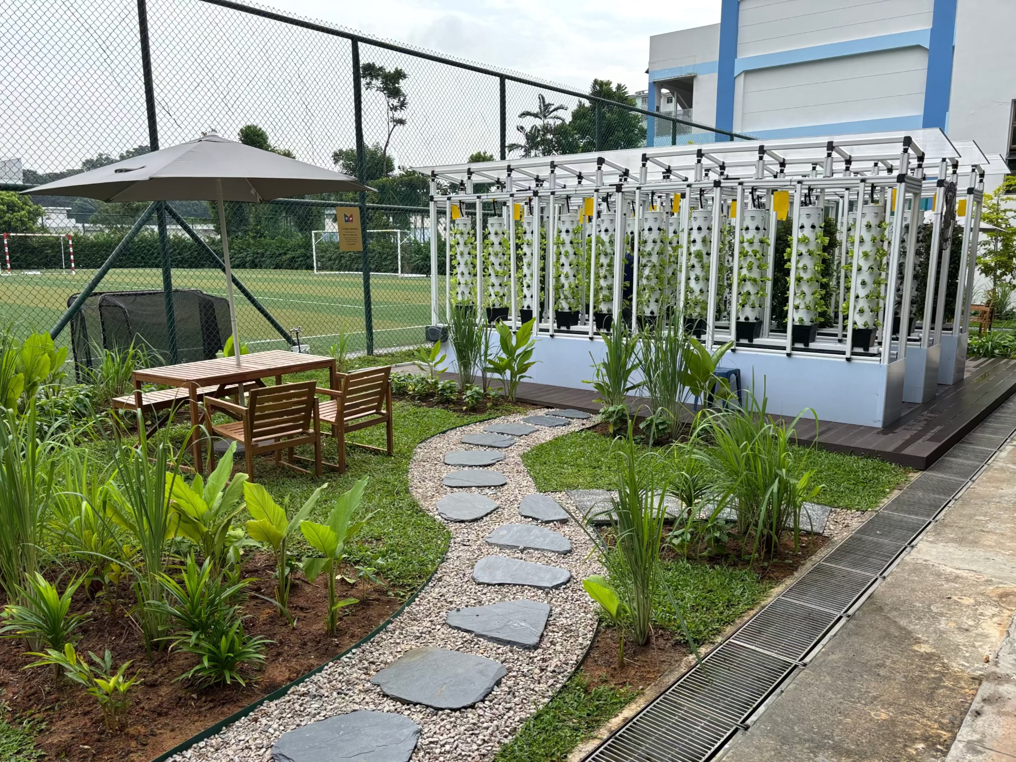 Outdoor garden with hydroponic system, table, and chairs near a building.